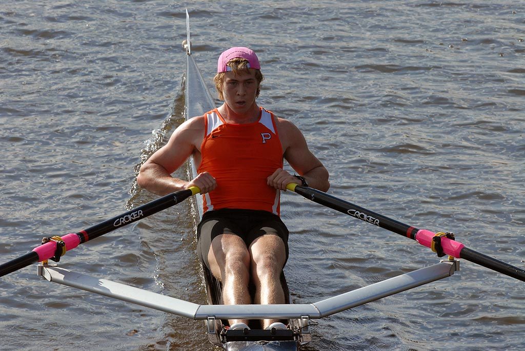 A man wearing a red and white rowing a boat in the water